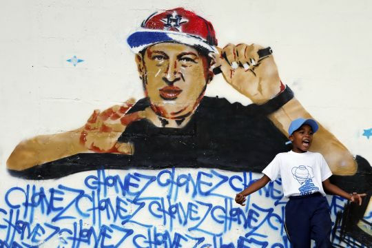 Boy plays next to graffiti depicting Venezuelan President Hugo Chavez as a rap singer in Petare in the suburbs of Caracas