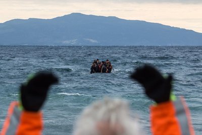 Un voluntario hace señas a una barca llena de refugiados frente a la isla griega de Lesbos.