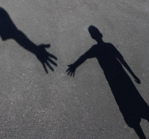 Helping Hand with a shadow on pavement of an adult hand offering help or therapy to a child in need as an education concept of charity towards needy kids and teacher guidance to students who need tutoring.