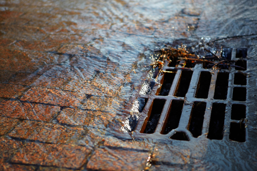 Melted water flows down through the manhole cover on a sunny spring day