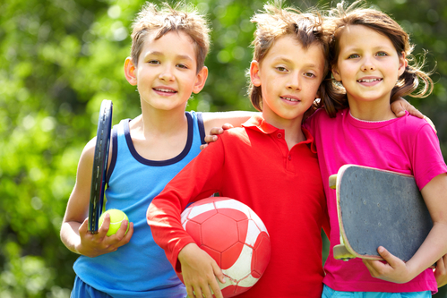 Portrait of three embracing children with sports equipment